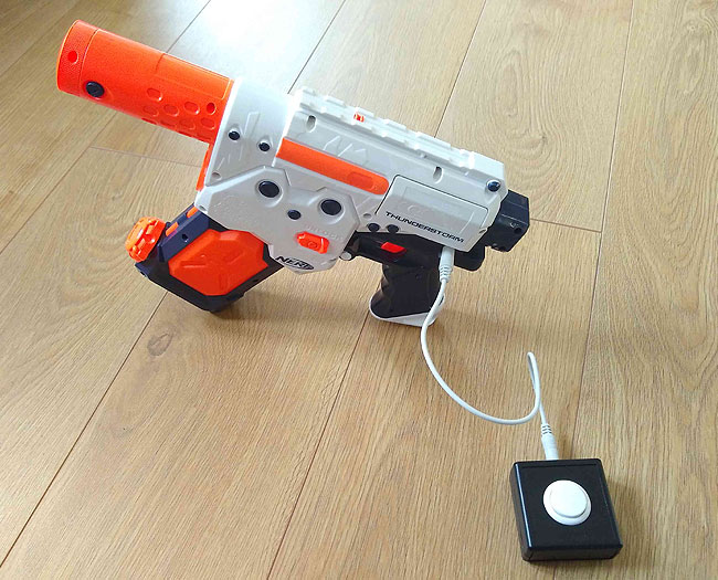 Switch adapted NERF Thunderstorm battery powered water pistol, standing up, with a small SANWA switch plugged in.