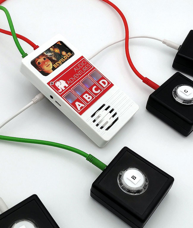 A Truman Toys Audio Adventures games machine. A,B,C,D buttons and lights above. Bewilder game cartridge fitted at the top and four leads coming out of the back connected to accessibility switches.
