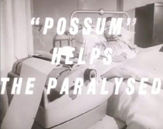 Possum Helps The Paralysed.  Black and white still from a short 1960s film from Possum. The image is of a man in pyjamas lying in bed, looking towards an electric typewriter.   White italic text overlays this scene, reading, Possum Helps the Paralysed.