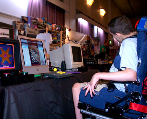 Accessible Gaming Museum. Chris Myers playing one-switch accessible Shenmue Darts at a gaming convention.